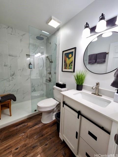 full bath featuring toilet, vanity, a marble finish shower, and wood finished floors