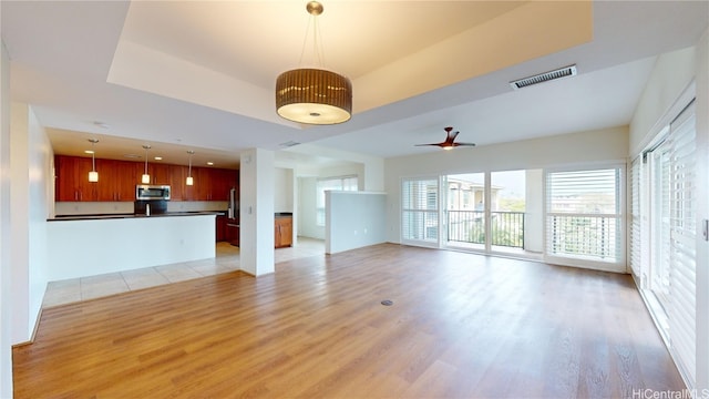 unfurnished living room with light wood-style flooring, a raised ceiling, visible vents, and a ceiling fan