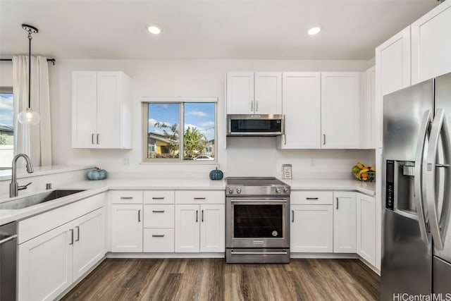 kitchen with a sink, white cabinetry, light countertops, appliances with stainless steel finishes, and dark wood-style floors