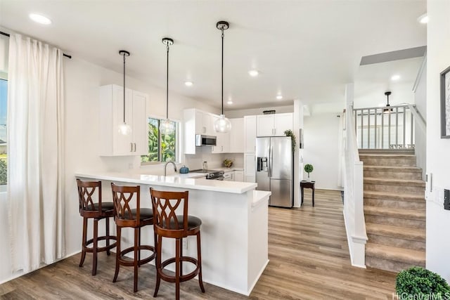 kitchen with stainless steel appliances, light countertops, light wood-style floors, a peninsula, and a kitchen bar