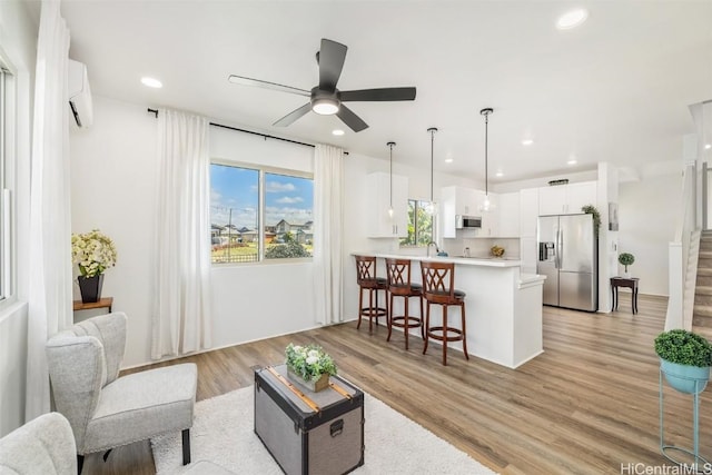 living room featuring recessed lighting, light wood-style flooring, a wall mounted AC, ceiling fan, and stairs