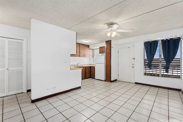 kitchen featuring ceiling fan, a textured ceiling, baseboards, light countertops, and freestanding refrigerator