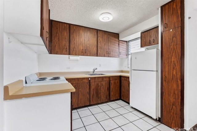 kitchen with light tile patterned floors, a textured ceiling, a sink, light countertops, and freestanding refrigerator