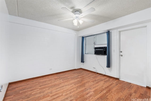 empty room featuring light wood-style floors, ceiling fan, a textured ceiling, and cooling unit