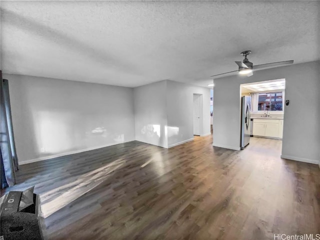 unfurnished living room with a ceiling fan, a sink, a textured ceiling, wood finished floors, and baseboards