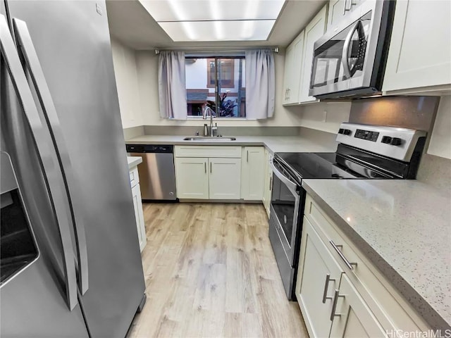 kitchen with light stone counters, stainless steel appliances, light wood-style flooring, white cabinets, and a sink