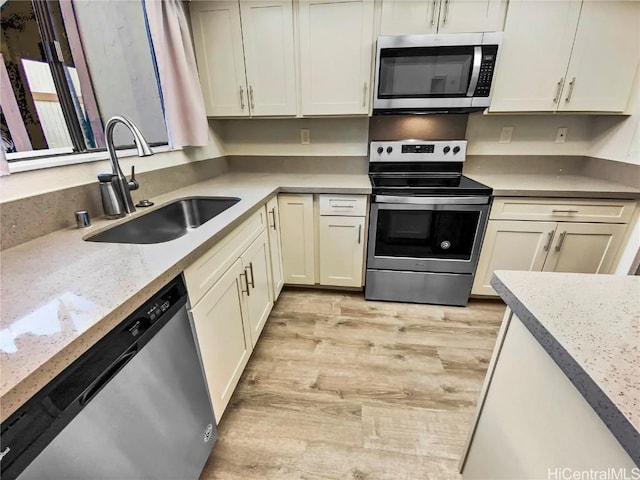 kitchen featuring light stone countertops, light wood-style floors, appliances with stainless steel finishes, and a sink