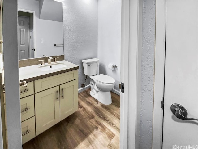 bathroom with baseboards, a textured wall, toilet, wood finished floors, and vanity