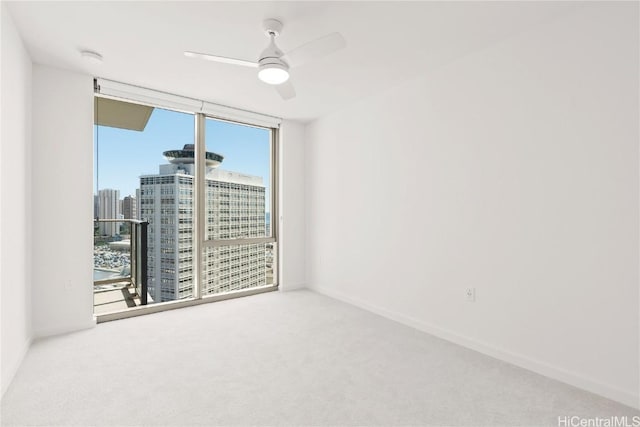 spare room featuring ceiling fan, baseboards, a view of city, a wall of windows, and carpet