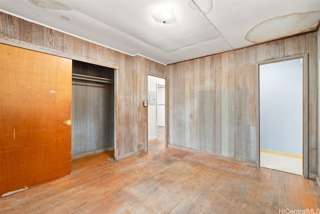 unfurnished bedroom with a closet, wood-type flooring, and wooden walls