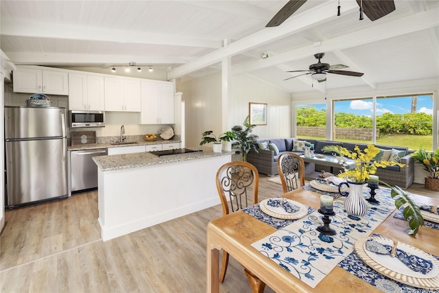 kitchen featuring white cabinetry, a sink, appliances with stainless steel finishes, lofted ceiling with beams, and light wood-type flooring