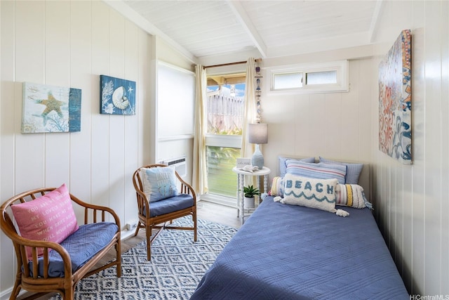bedroom with wooden walls, wood finished floors, and beamed ceiling