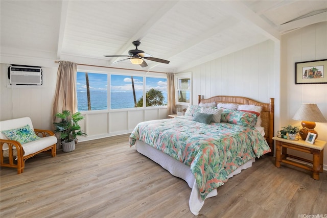 bedroom with a wall unit AC, beam ceiling, a water view, a ceiling fan, and wood finished floors