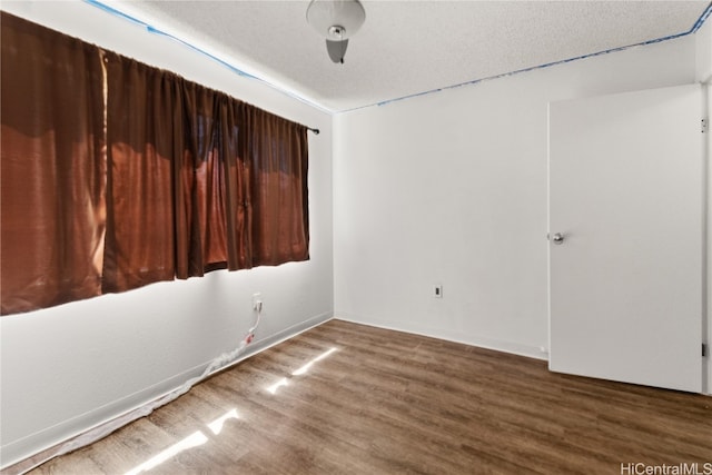 spare room with a textured ceiling, wood finished floors, and baseboards