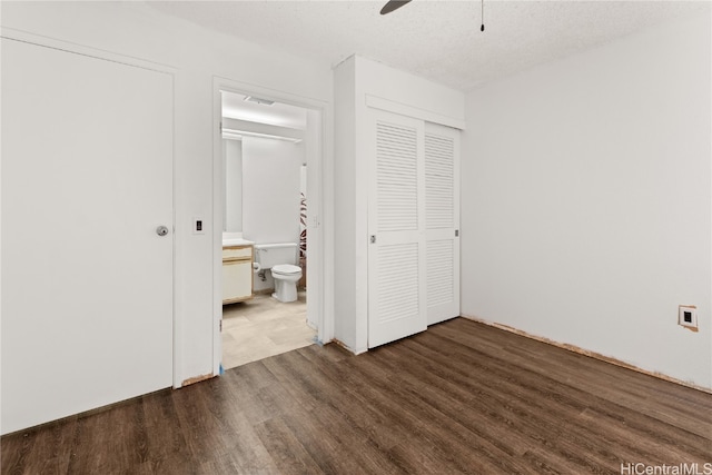 unfurnished bedroom with a textured ceiling, connected bathroom, dark wood-type flooring, a ceiling fan, and a closet