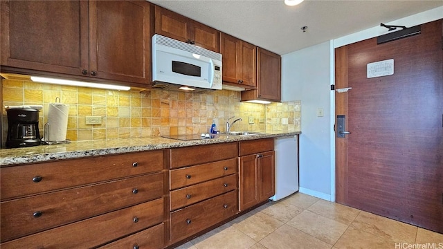 kitchen featuring light stone counters, light tile patterned floors, backsplash, a sink, and white appliances