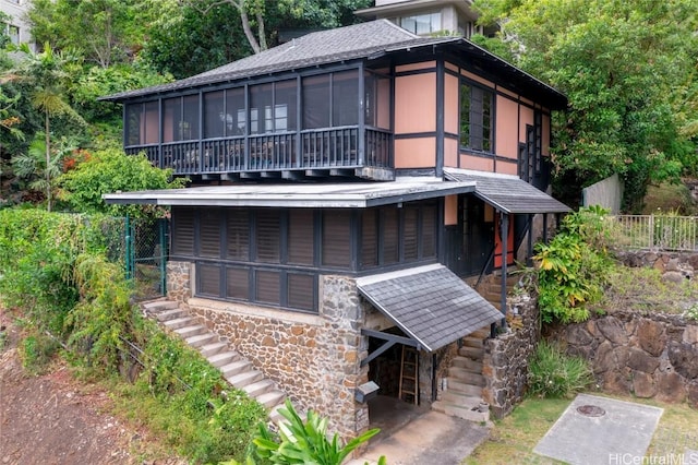 view of front of home with stone siding, a sunroom, roof with shingles, and fence