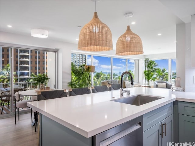 kitchen featuring open floor plan, a sink, light countertops, pendant lighting, and stainless steel dishwasher