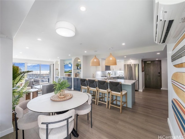 dining space featuring a wall unit AC, baseboards, wood finished floors, and recessed lighting