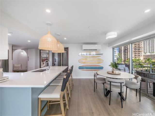 kitchen featuring a wall unit AC, recessed lighting, hanging light fixtures, a sink, and wood finished floors