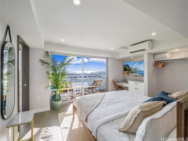 bedroom with a wall unit AC, light wood-style flooring, recessed lighting, baseboards, and access to outside