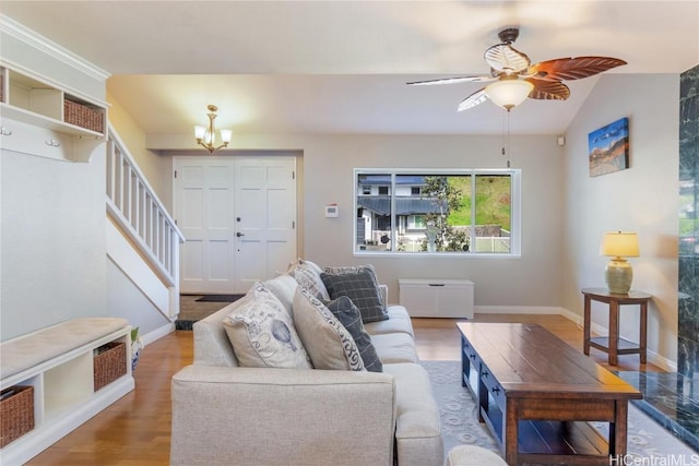 living area featuring lofted ceiling, ceiling fan with notable chandelier, wood finished floors, baseboards, and stairs