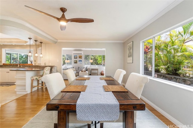 dining space featuring light wood-type flooring, crown molding, a wall unit AC, and a wealth of natural light