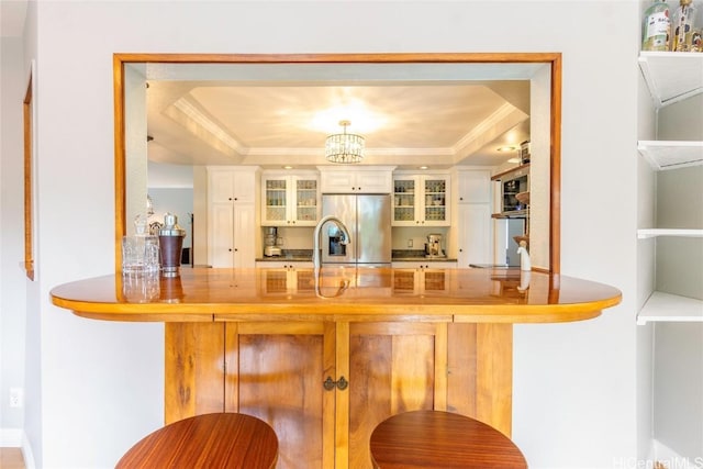 bar with ornamental molding, a raised ceiling, a notable chandelier, and stainless steel fridge with ice dispenser