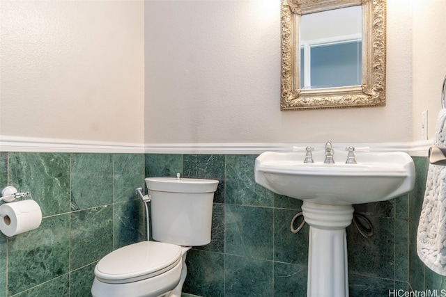 half bath featuring wainscoting, toilet, and tile walls