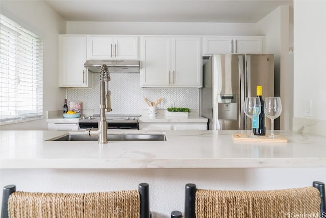 kitchen featuring a breakfast bar area, tasteful backsplash, white cabinetry, stainless steel fridge, and under cabinet range hood