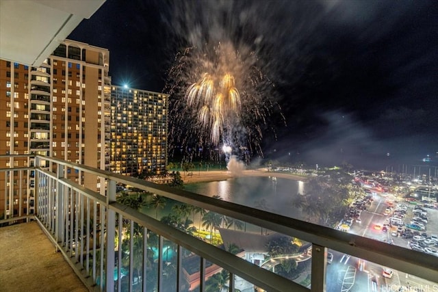 balcony at night featuring a view of city lights and a water view