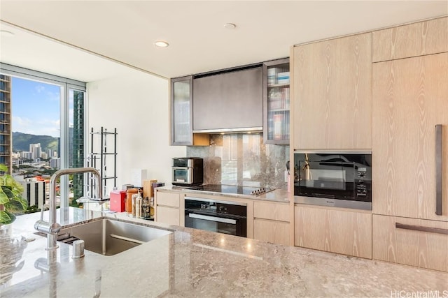 kitchen featuring a sink, light brown cabinetry, light stone counters, black appliances, and modern cabinets