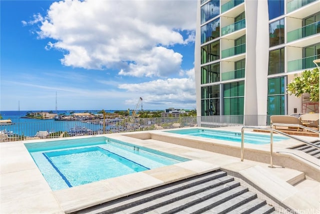 community pool featuring a patio area, fence, a community hot tub, and a water view