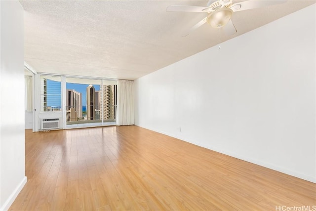 empty room featuring light wood-style floors, a ceiling fan, a textured ceiling, a wall of windows, and baseboards