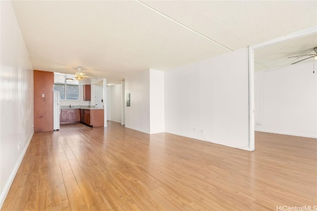 unfurnished living room with light wood-type flooring, baseboards, and a ceiling fan