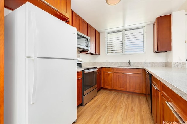 kitchen featuring brown cabinets, light countertops, appliances with stainless steel finishes, a sink, and light wood-type flooring