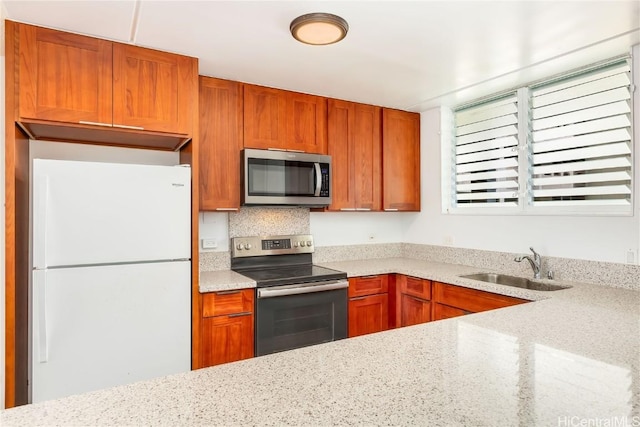 kitchen with stainless steel appliances, brown cabinets, a sink, and light stone countertops