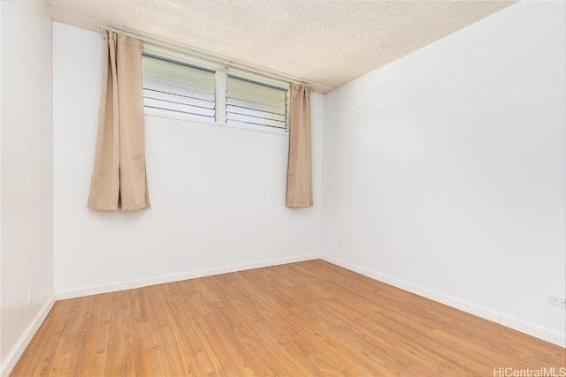 spare room with baseboards, a textured ceiling, and light wood finished floors