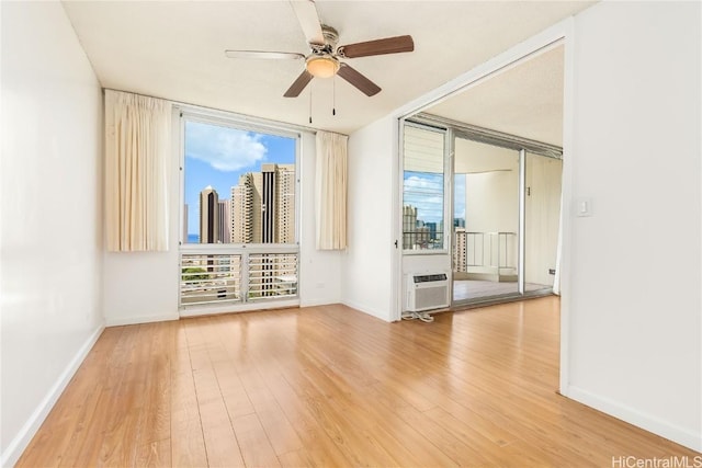 empty room featuring wood finished floors, floor to ceiling windows, ceiling fan, and a wall mounted AC