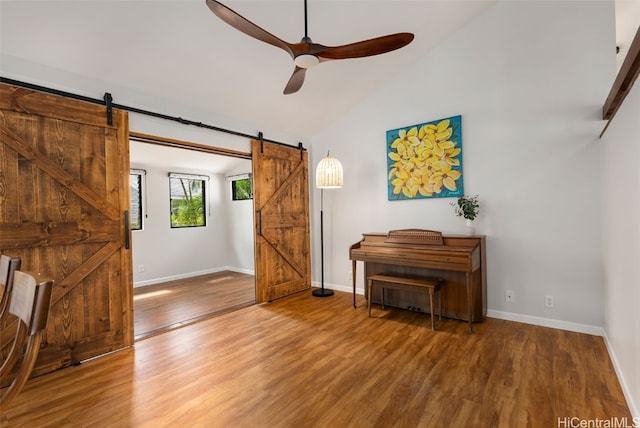 living area with a ceiling fan, a barn door, wood finished floors, and baseboards