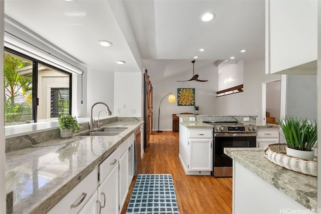 kitchen featuring stainless steel electric range oven, a barn door, light wood-style floors, white cabinets, and a sink