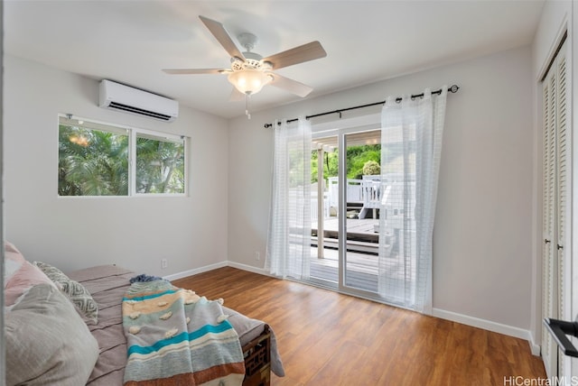 bedroom featuring access to exterior, wood finished floors, baseboards, and a wall mounted air conditioner