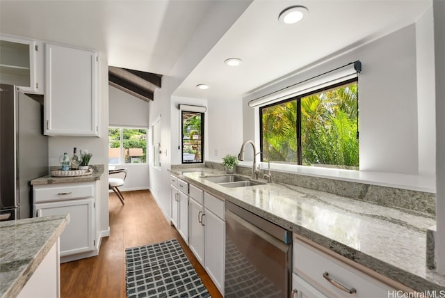 kitchen featuring light stone countertops, light wood-style flooring, stainless steel appliances, white cabinetry, and a sink