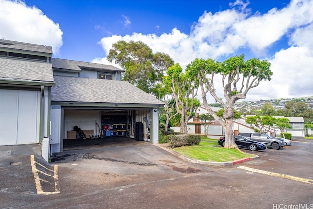 exterior space featuring a garage, uncovered parking, and roof with shingles