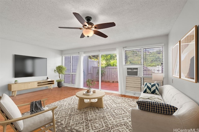 living area with a ceiling fan, cooling unit, a textured ceiling, and wood finished floors