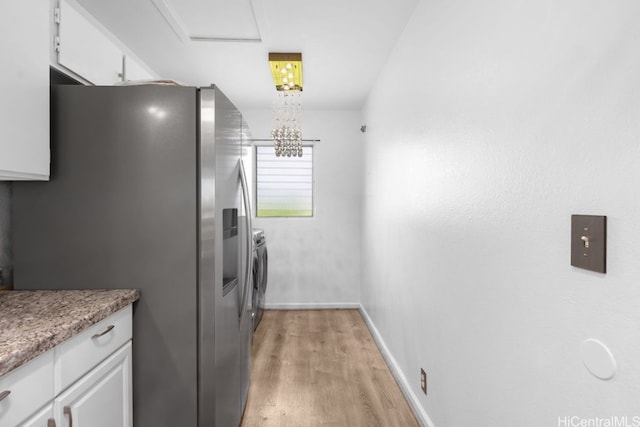 kitchen with baseboards, white cabinetry, light wood-style flooring, washer and dryer, and stainless steel fridge