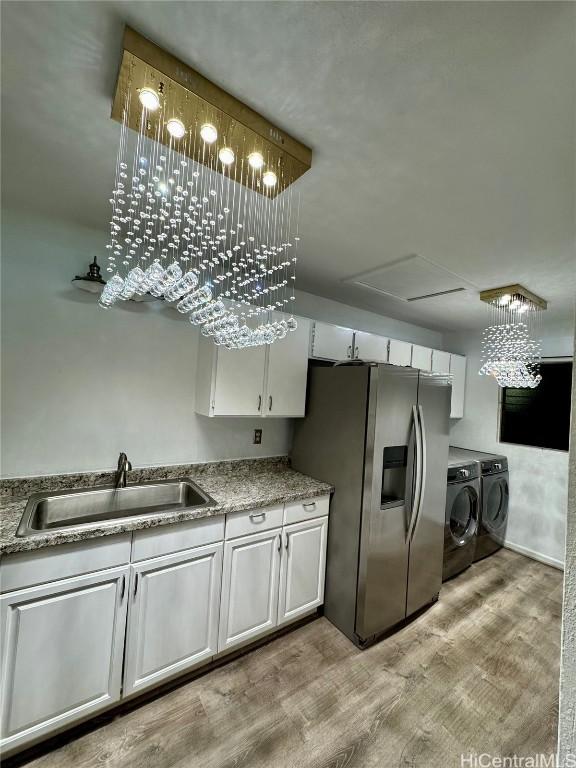 kitchen featuring a sink, stainless steel fridge, white cabinets, washing machine and dryer, and light wood-type flooring