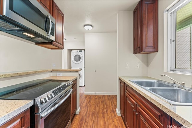 kitchen with stainless steel appliances, light countertops, a sink, stacked washing maching and dryer, and wood finished floors