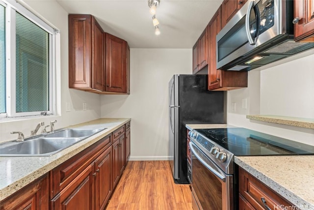 kitchen with light wood finished floors, baseboards, appliances with stainless steel finishes, light stone counters, and a sink