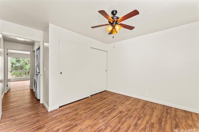 unfurnished bedroom featuring a closet, baseboards, stacked washing maching and dryer, and wood finished floors